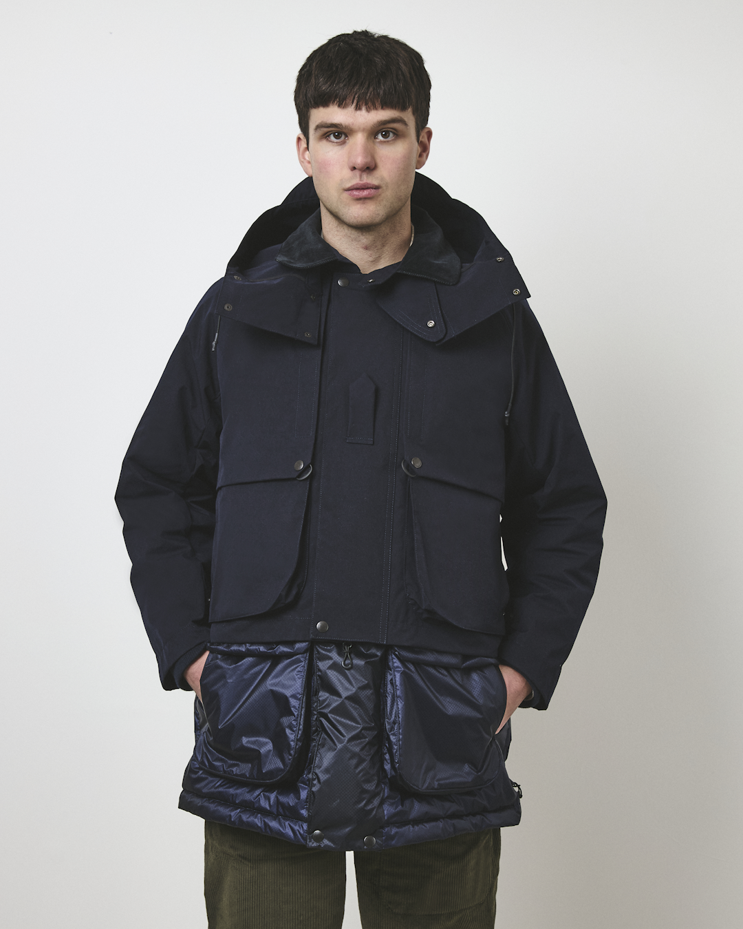 Studio photo of a man in a navy technical hooded jacket with quilted lower paneling.