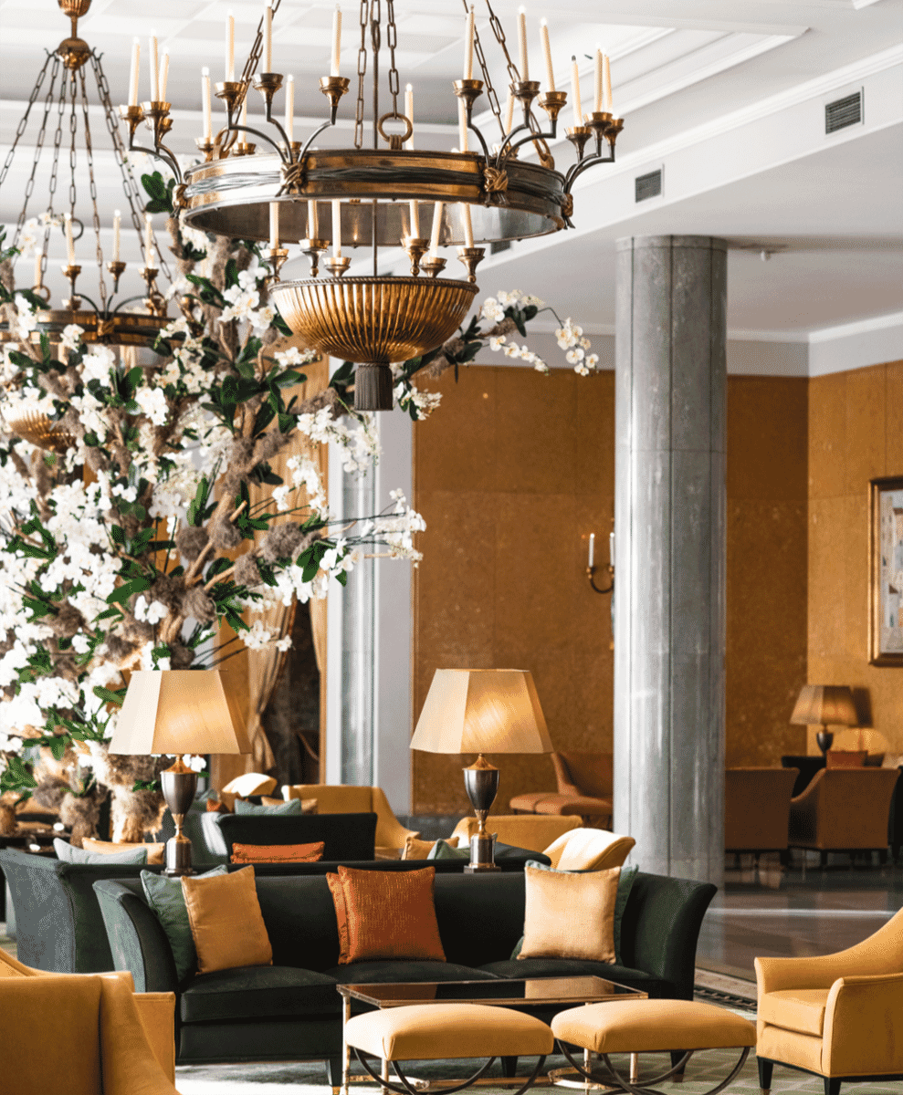 A luxurious hotel lobby with golden lighting, grand chandeliers, and plush furniture.