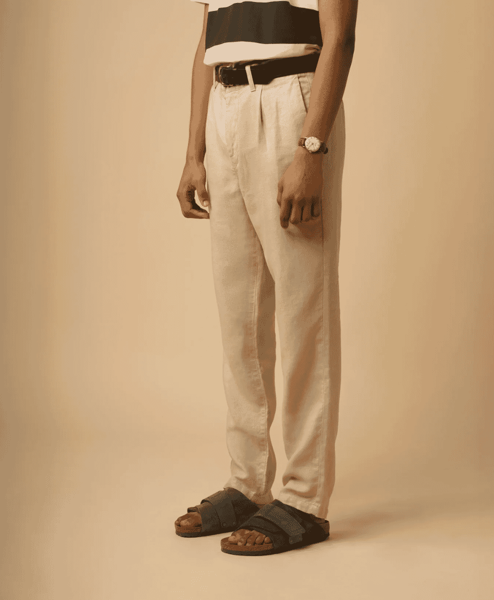 Detailed shot of a man wearing beige pleated trousers with a black-and-white striped shirt.