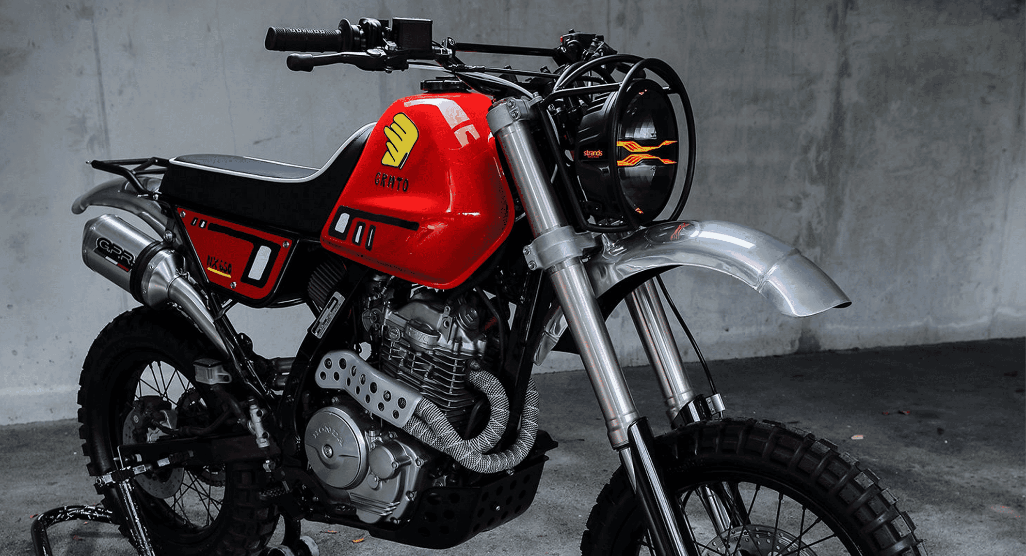 A custom red and black Honda NX650 street scrambler standing in a concrete industrial garage.