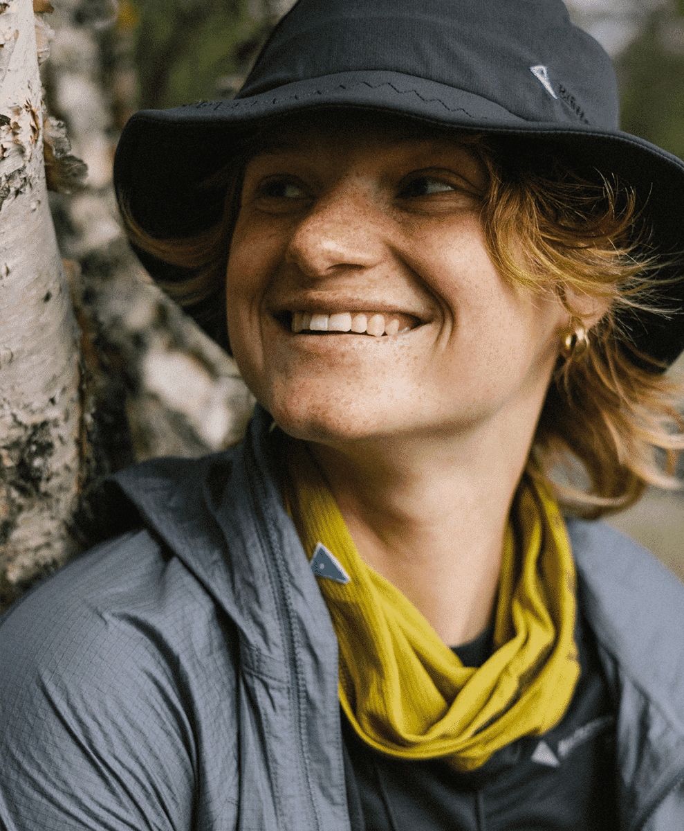 A person with freckles wearing a dark bucket hat and a bright yellow neck gaiter.