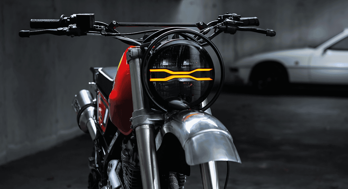 Close-up of a custom motorcycle's glowing orange LED headlight and red fuel tank.