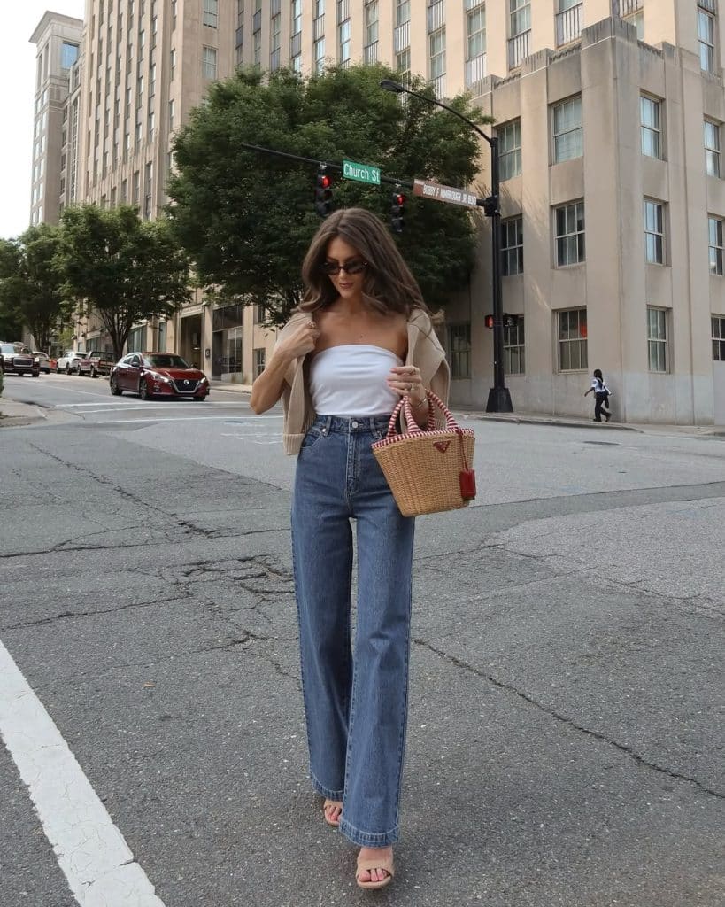 Woman in a white strapless top and beige blazer carrying a woven bag.