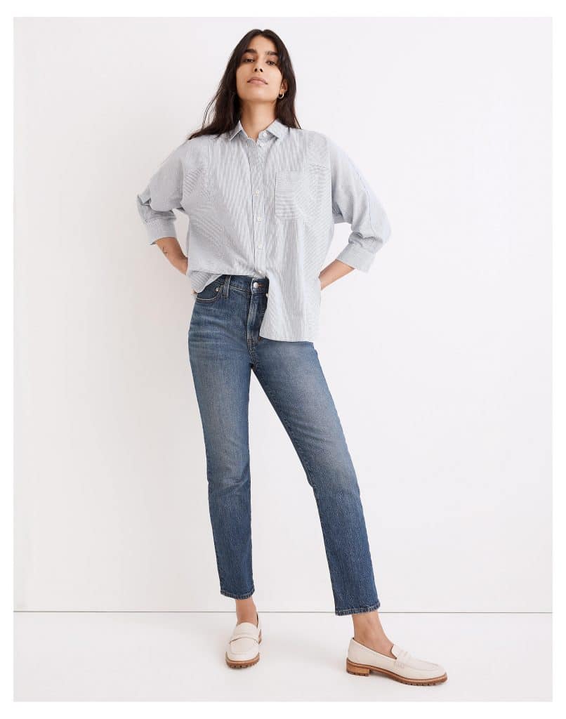 Woman in a light blue striped button-up shirt and denim jeans.