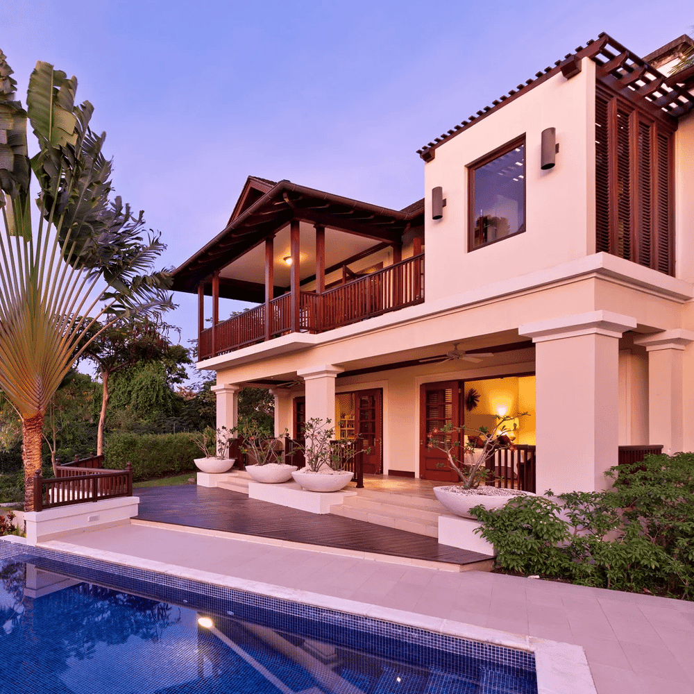 A luxury two-story wooden villa with a blue-tiled pool at dusk.