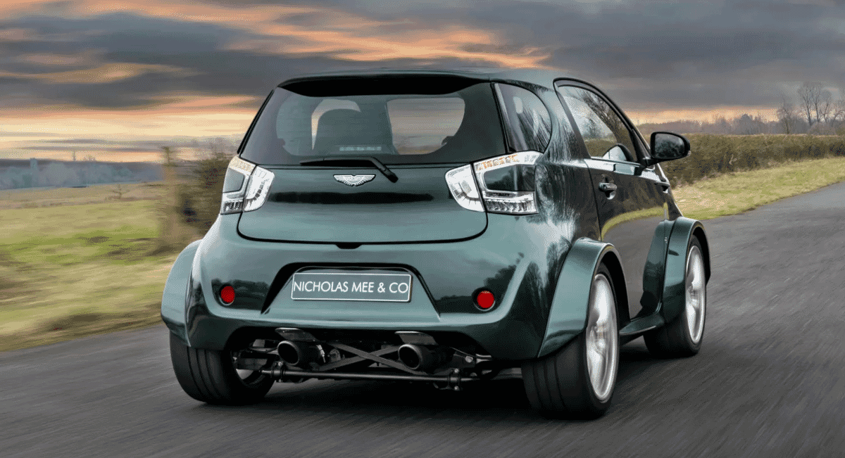 Rear-side view of a green Aston Martin Cygnet at sunset showing the custom exhaust system.