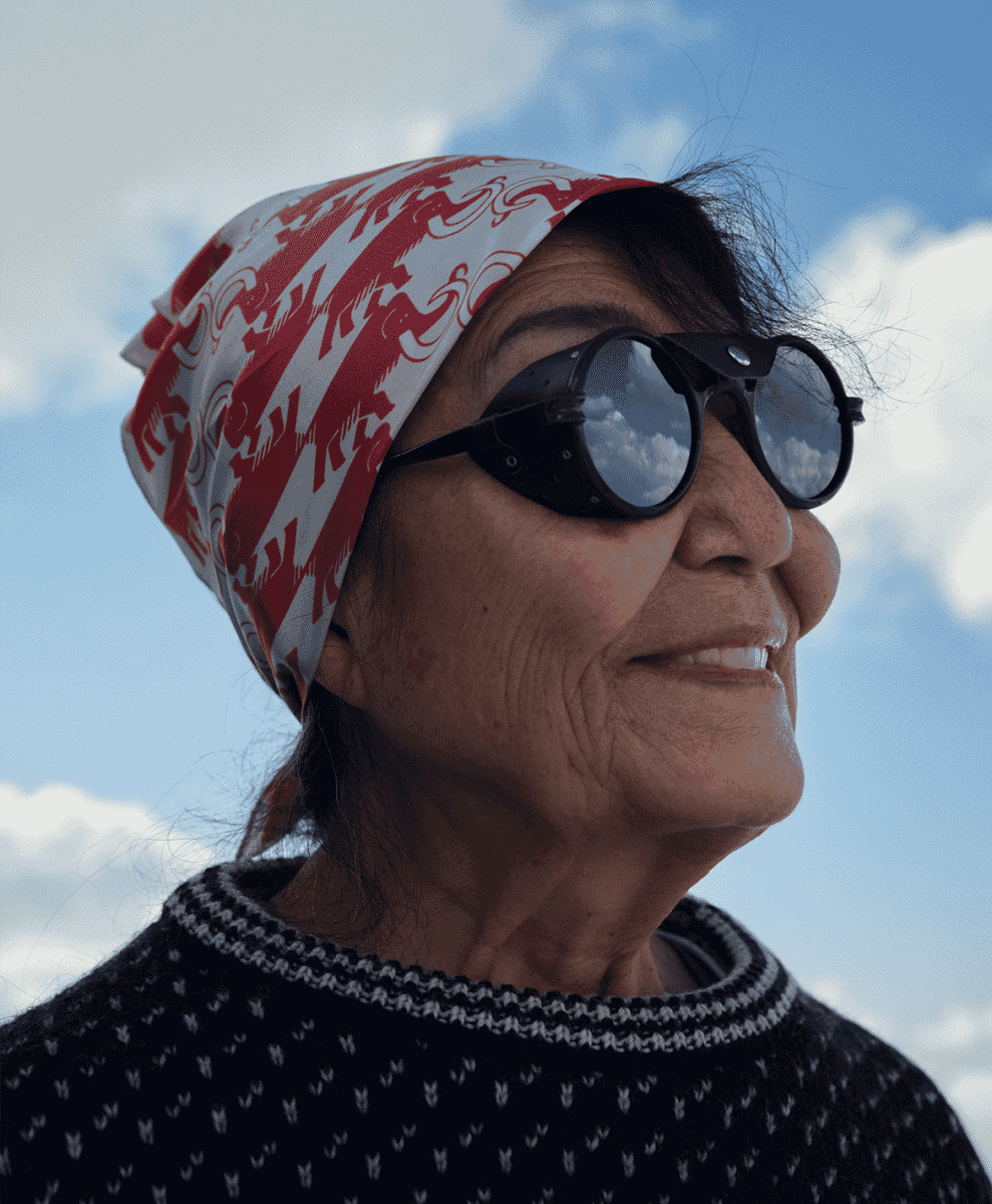 Portrait of Michiko Imai wearing a patterned headscarf, round sunglasses, and a dark knit sweater.