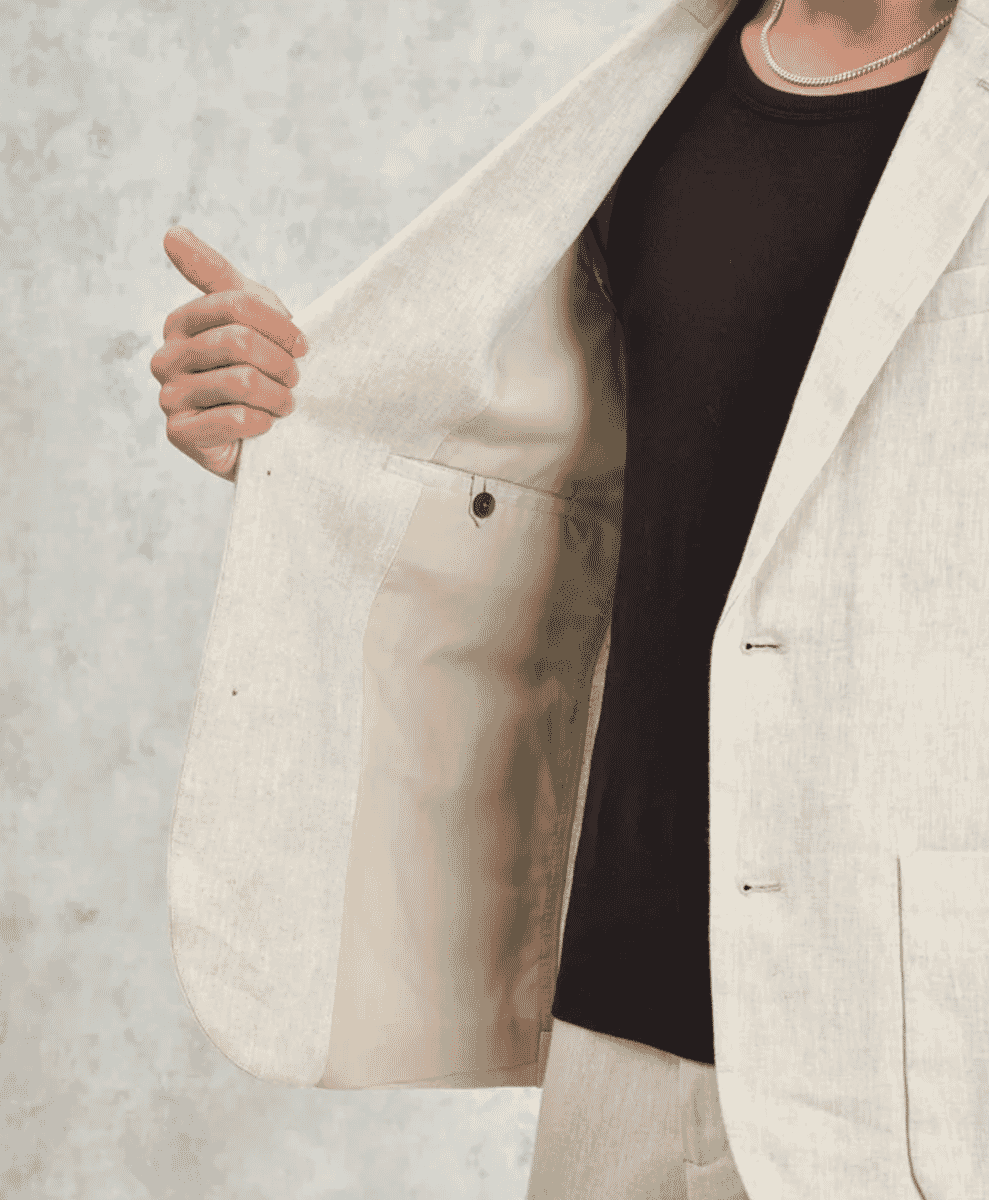 Man modeling a light beige linen blazer over a black t-shirt against a textured background.