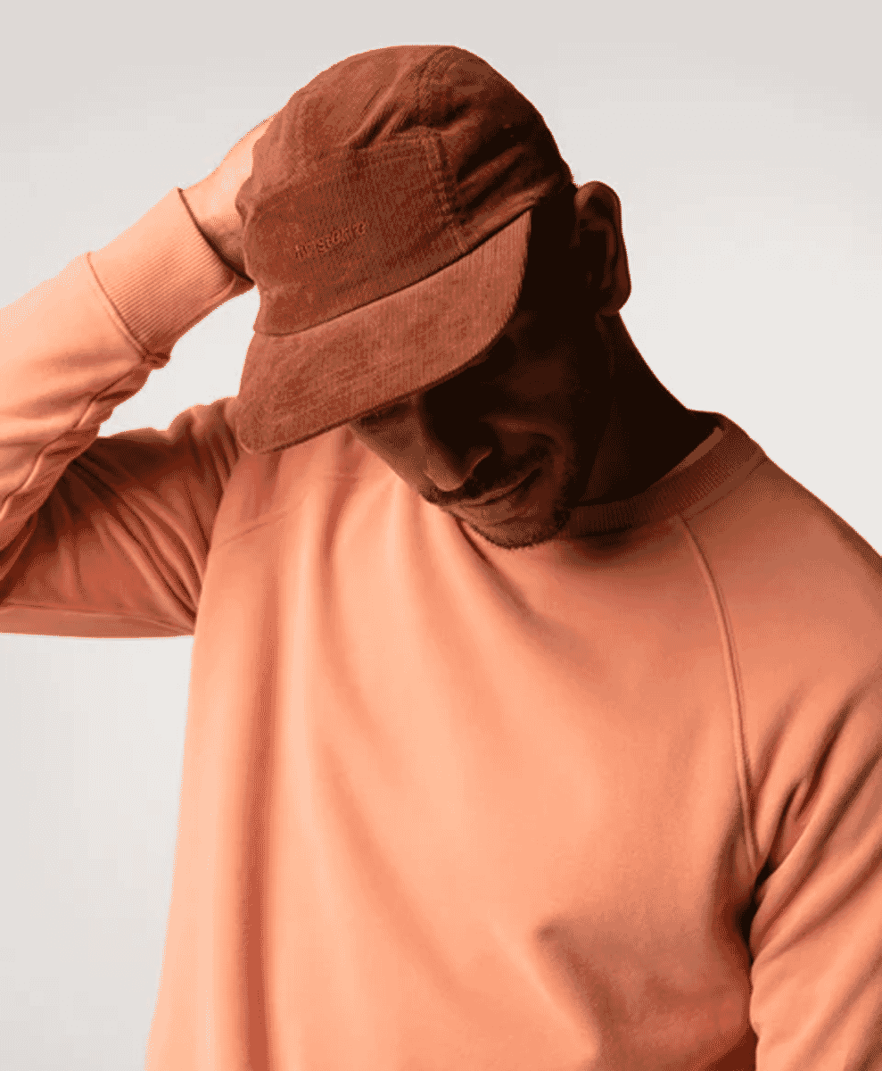 Model adjusting a brown corduroy cap while wearing a matching monochromatic sweatshirt.