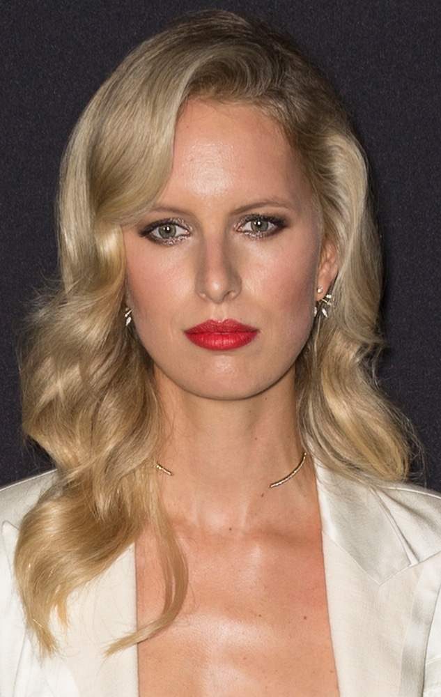 Claudia Schiffer with blonde wavy hair in a white blazer and bold red lipstick.