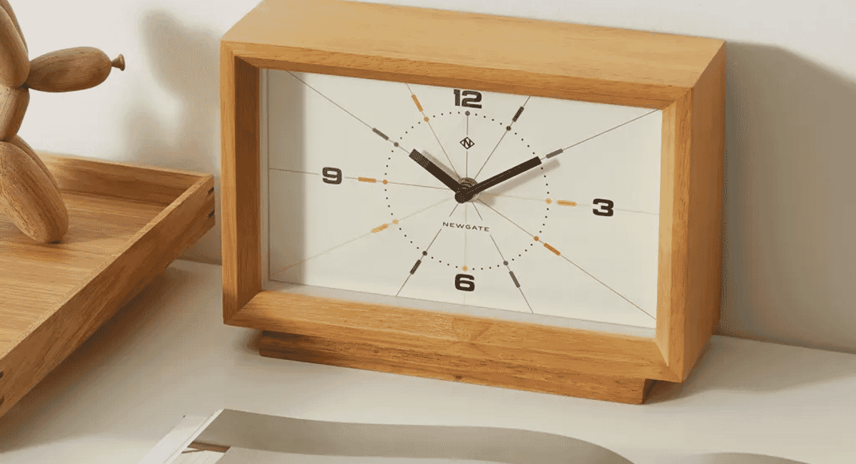 Minimalist wooden-framed analog clock on a neutral surface.