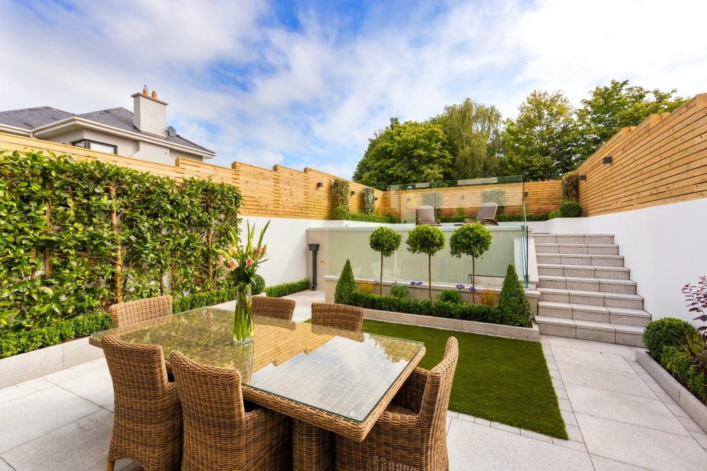 An outdoor patio area with a wicker dining set, glass table, and stone steps.