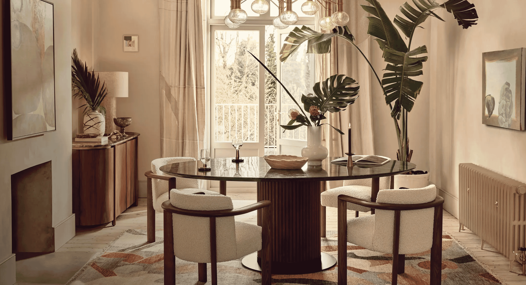 Modern dining room featuring a round marble table and lush tropical plants.