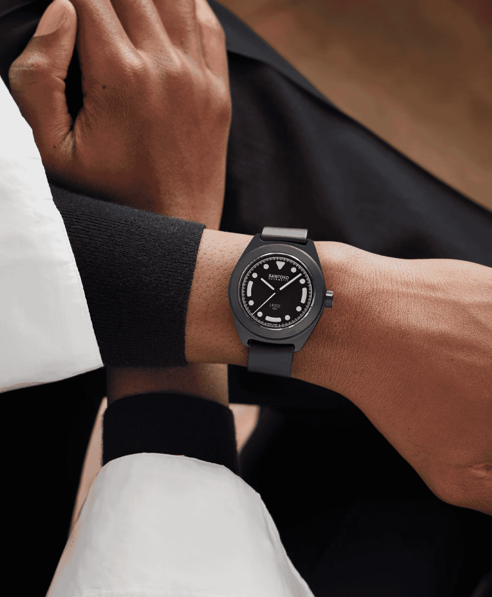 A minimalist black watch on a wrist paired with a white shirt and black sweater cuff.