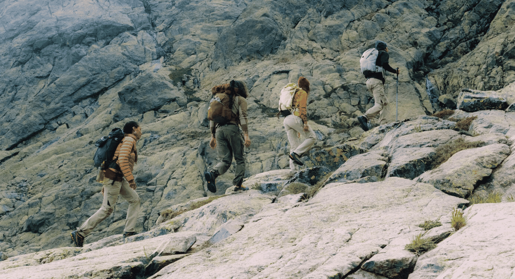 Four hikers wearing layered technical apparel trekking across a steep rocky slope.