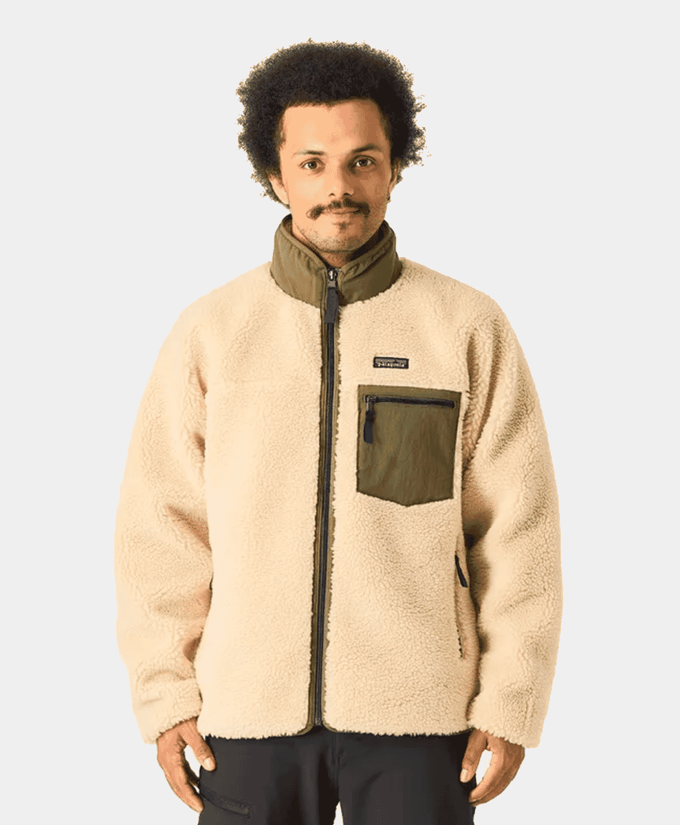 Model in a cream shearling jacket with olive green accents and front pocket.