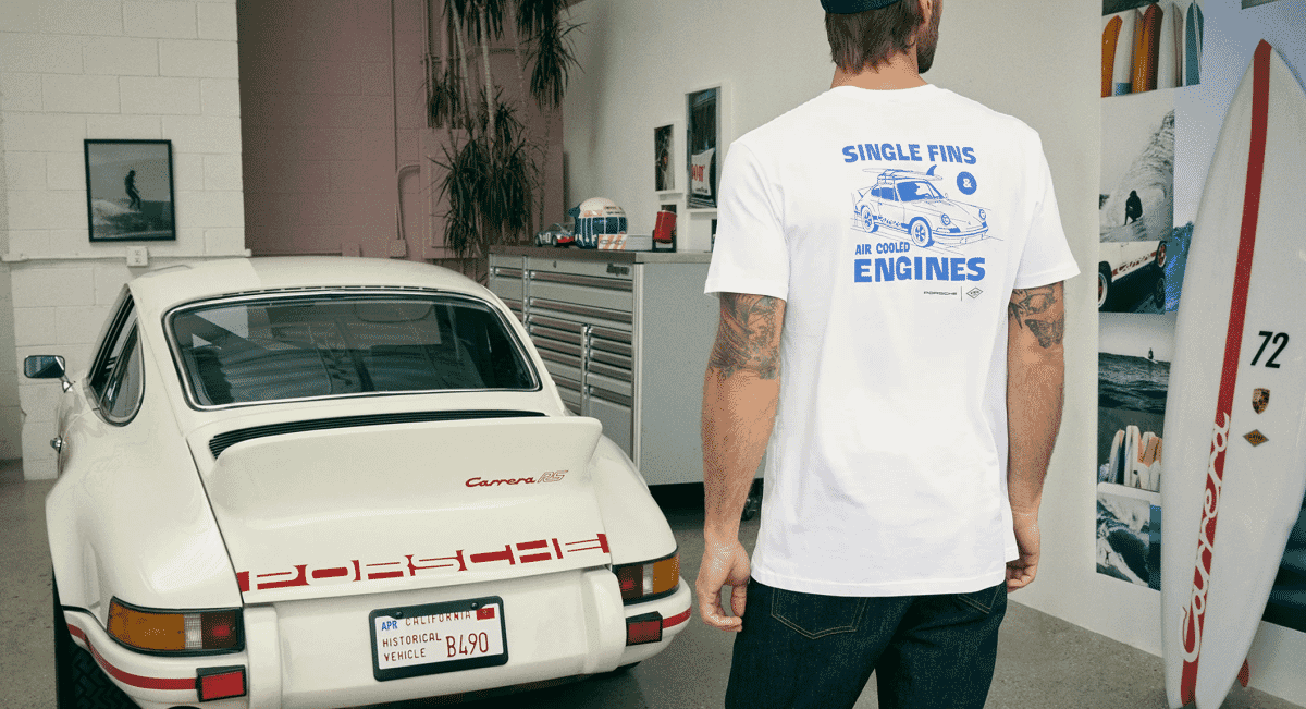 A man in a white Porsche graphic t-shirt standing next to a classic white Porsche Carrera RS.