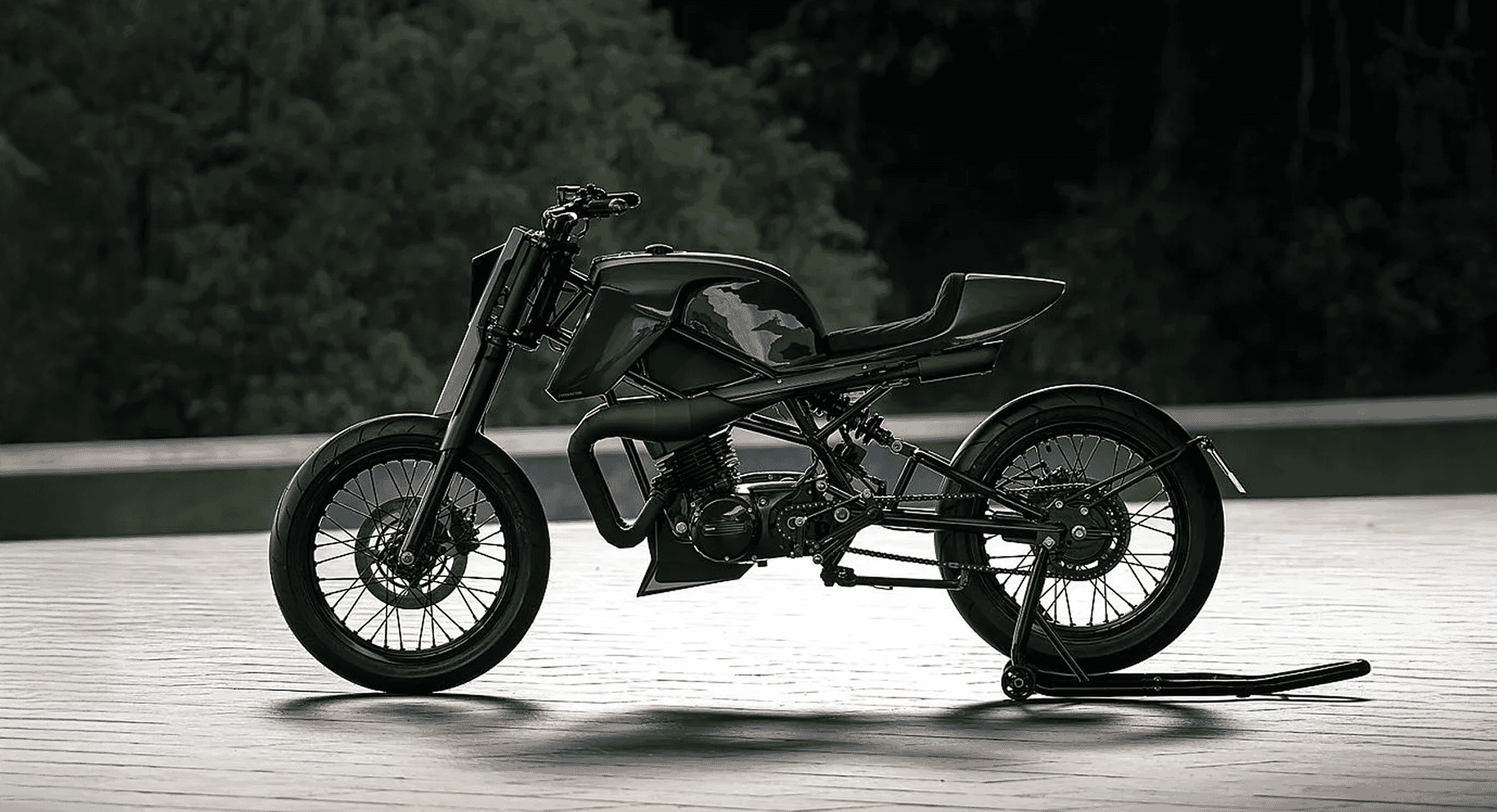 Full-bike shot of the custom Suzuki BS125 motorcycle on a wooden deck with a blurred natural background.