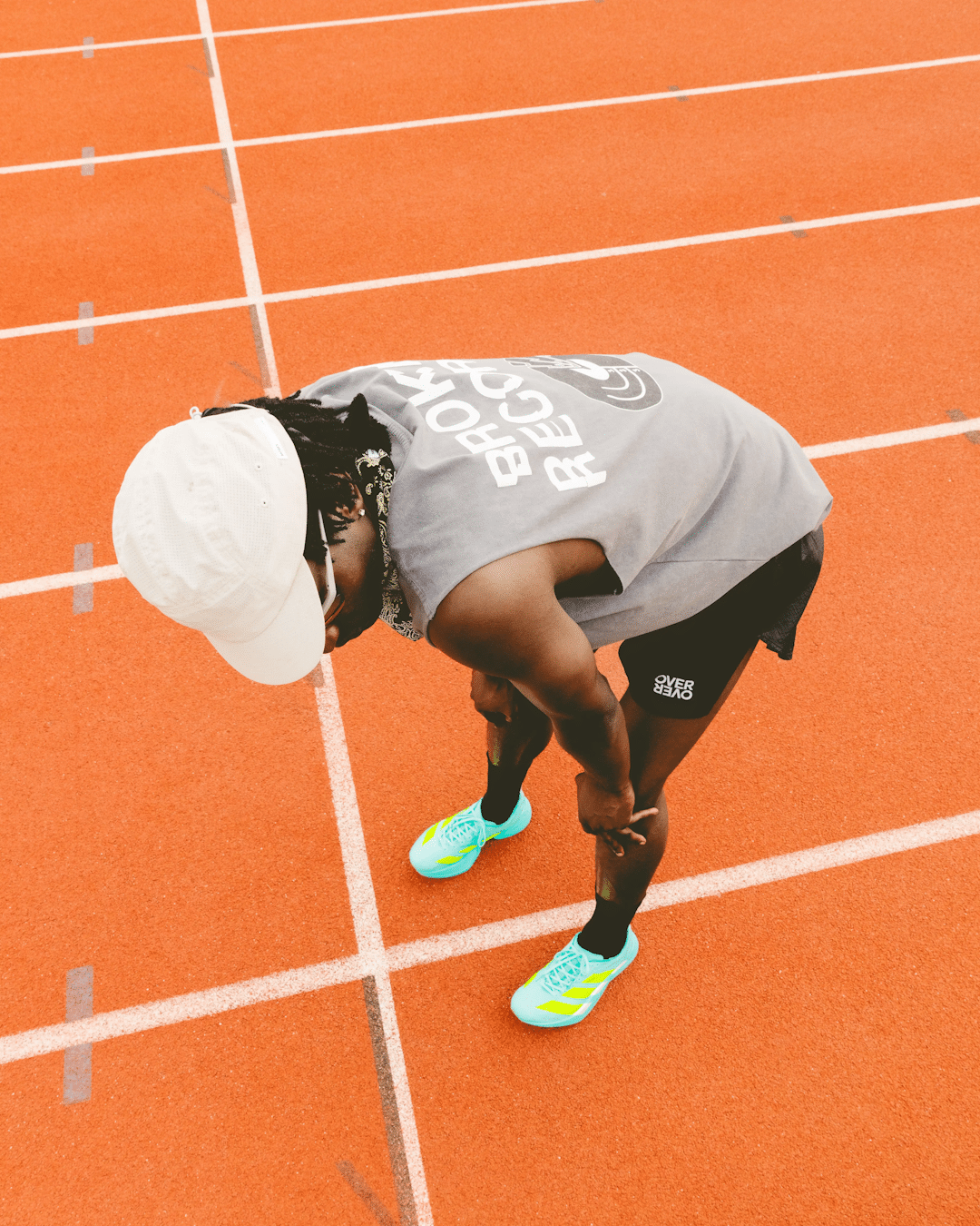 A runner in a gray sleeveless 'BROKEN RECORD' top and black shorts on an orange track.