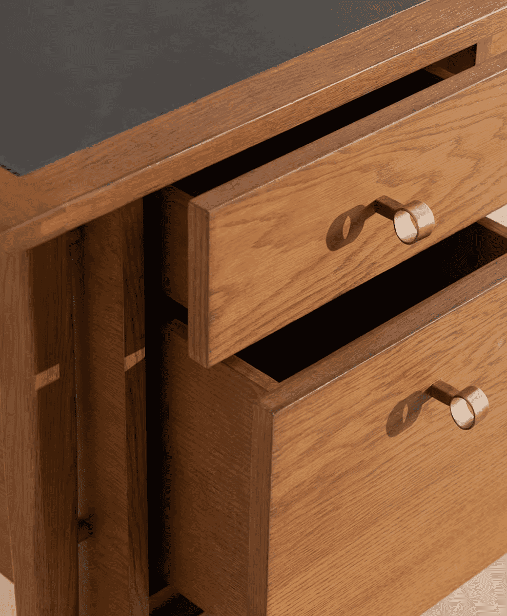 Close-up of a wooden desk drawer with metallic ring handles and natural wood grain.