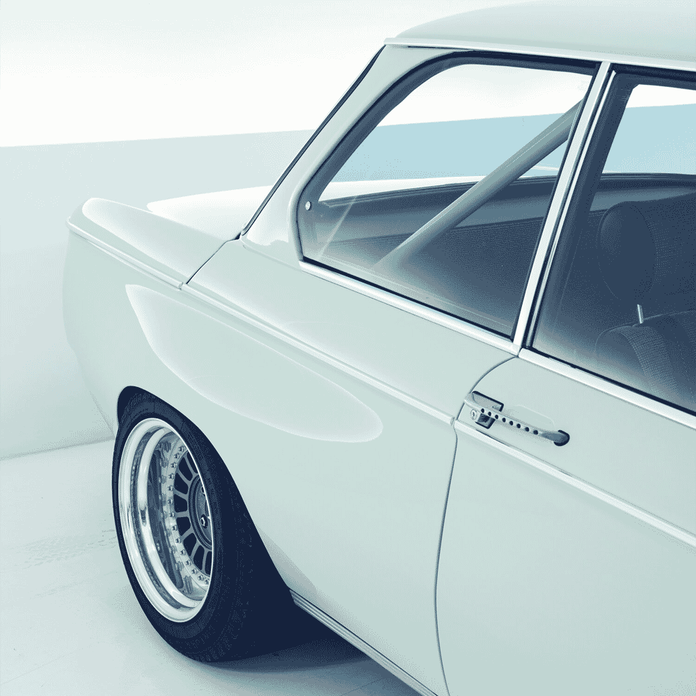 White vintage BMW with a custom roll cage visible through the windows and high-performance alloy wheels.