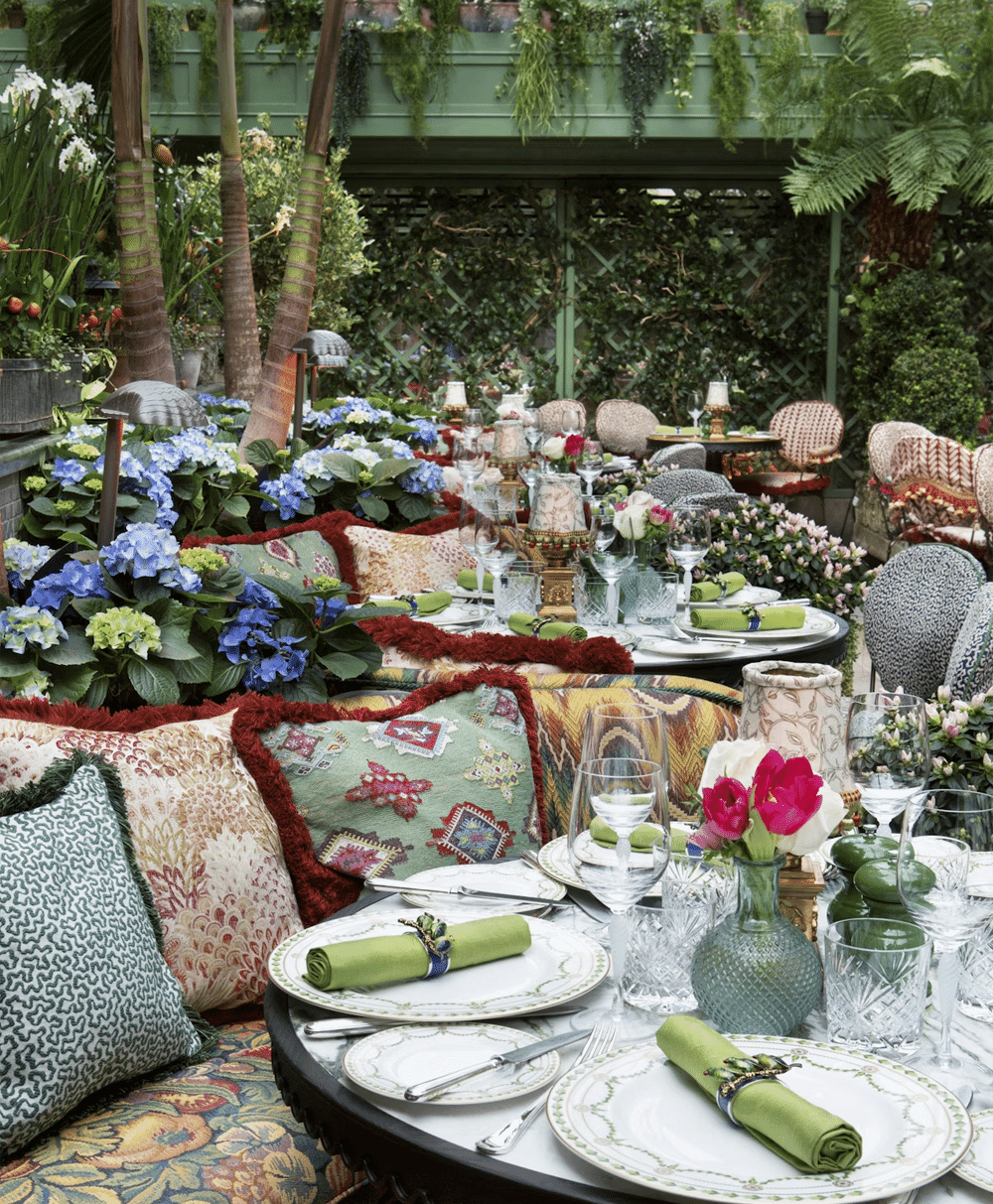 Luxury outdoor dining table set with green napkins, crystal glassware, and lush greenery.