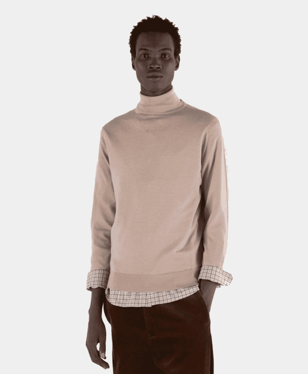 A model wearing a beige turtleneck sweater layered over a checkered shirt.