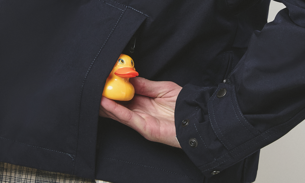 Detail shot of a yellow rubber duck tucked into the pocket of a navy technical jacket.