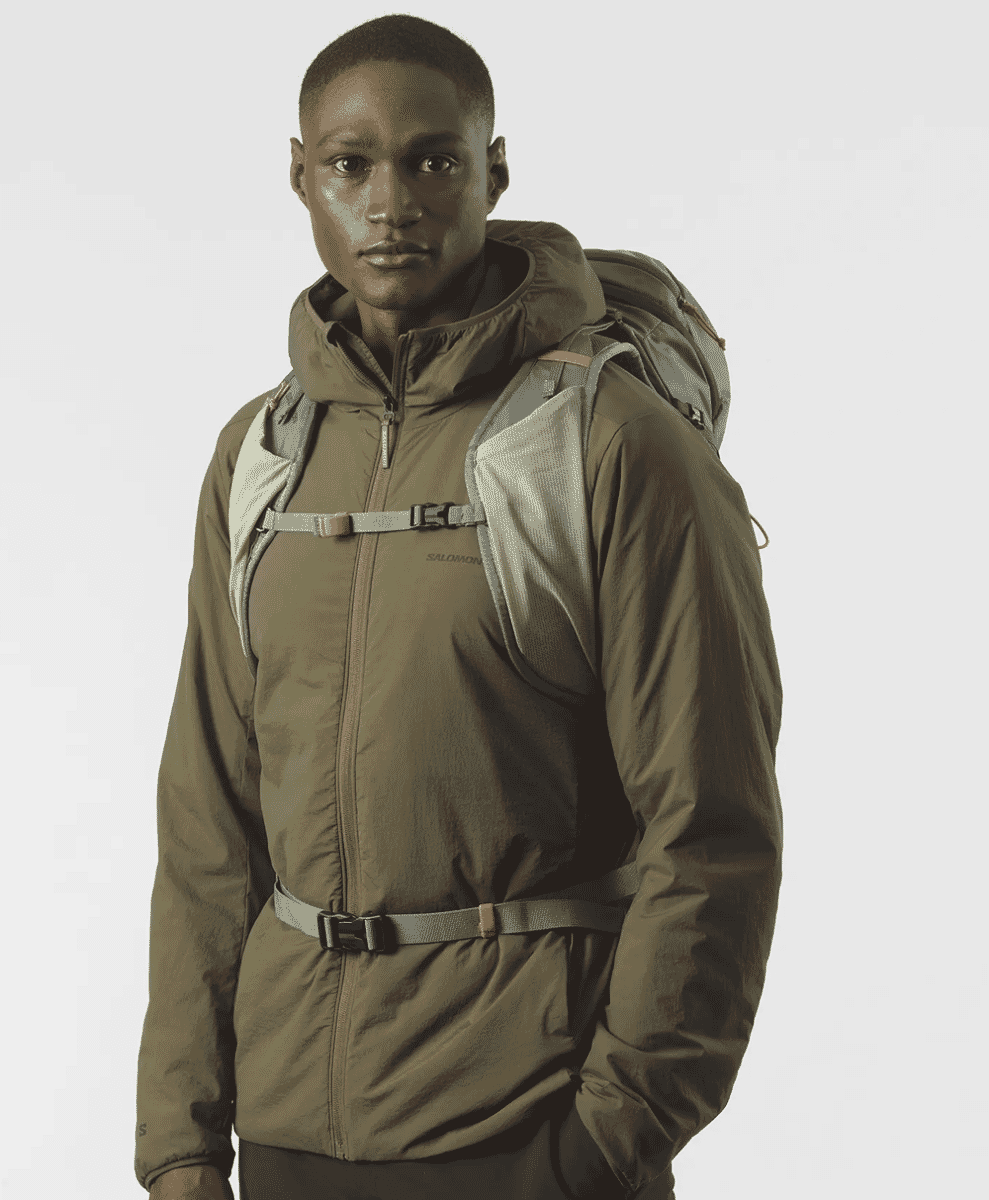 A model showcasing a technical brown Salomon jacket with integrated straps, designed for high-altitude functionality.
