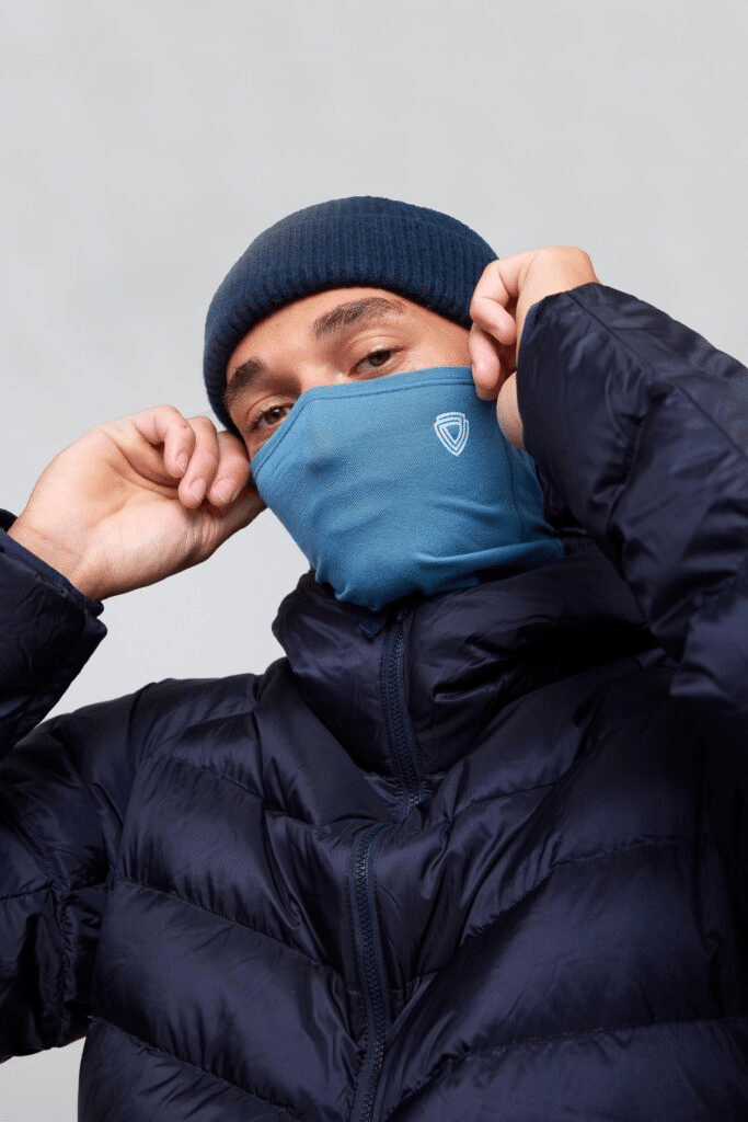 Man in a navy blue puffer jacket and matching beanie with a shield logo face mask.