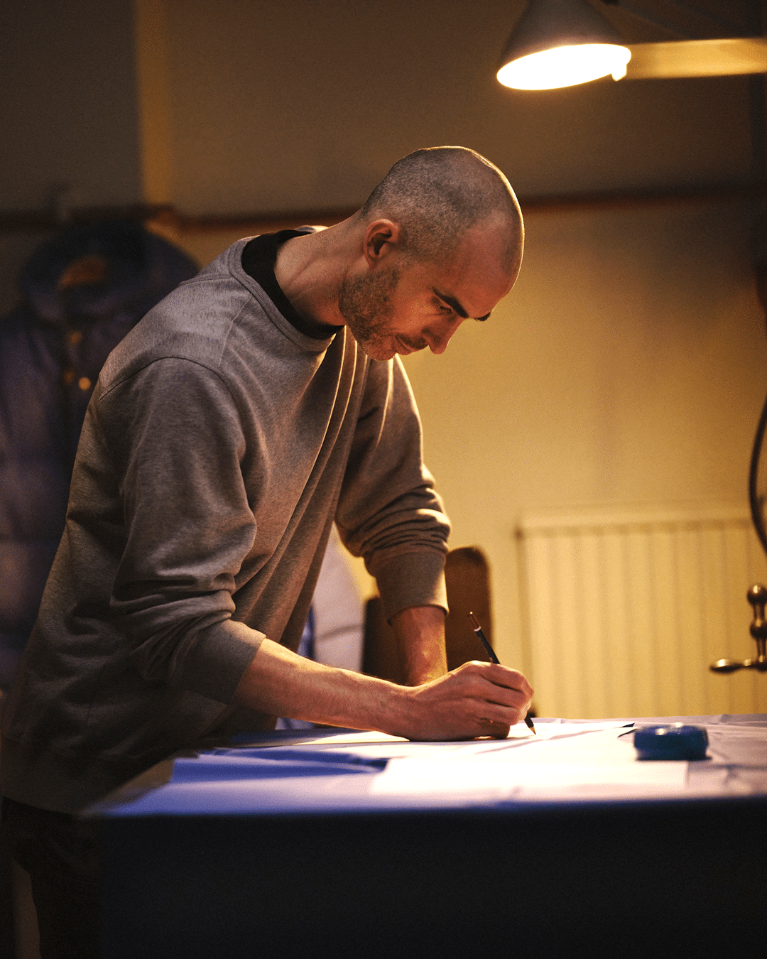 A designer in a gray sweatshirt sketching garment designs on paper in a studio.