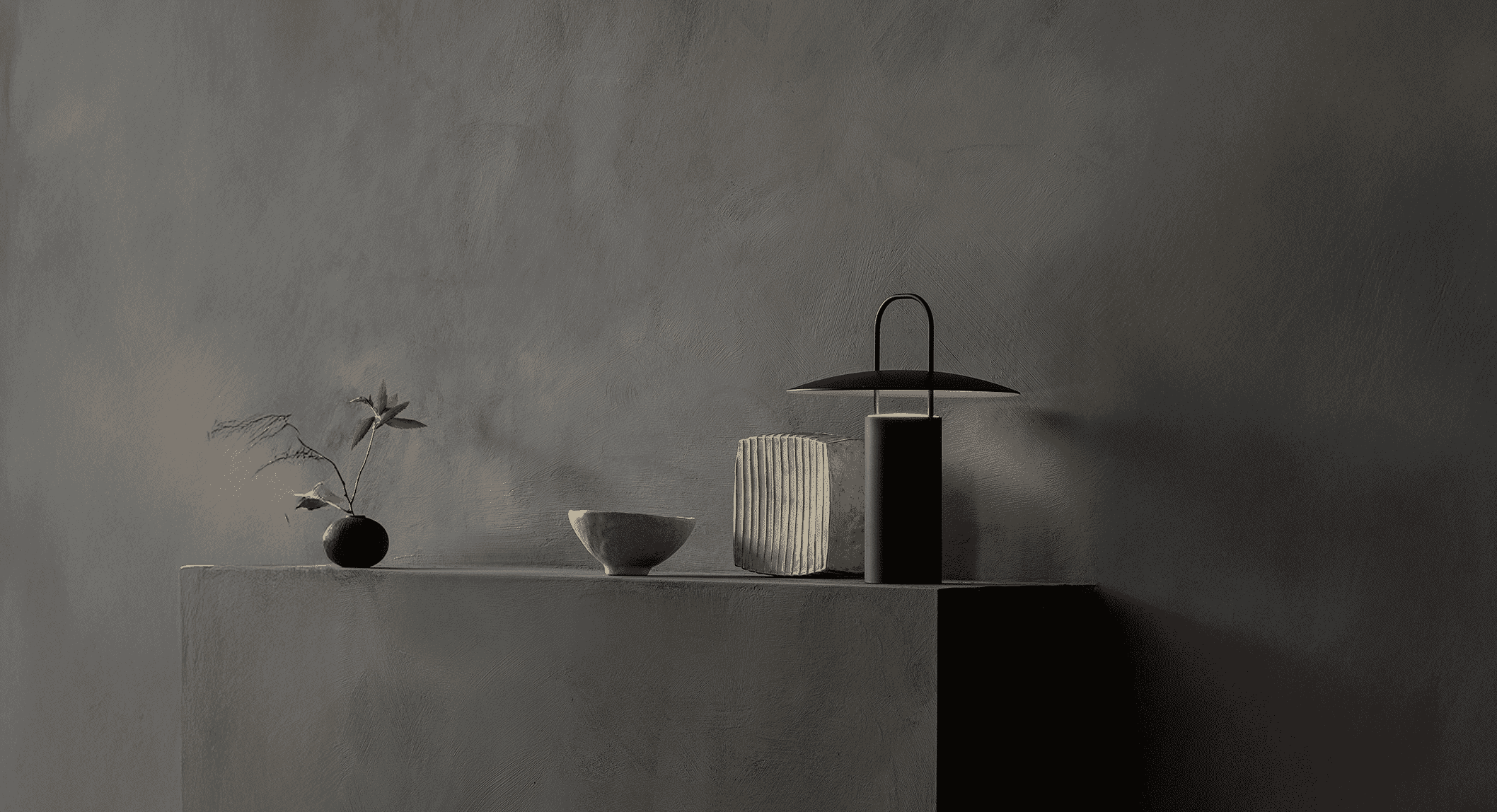 A monochromatic still life featuring a modern lamp on a textured concrete shelf.