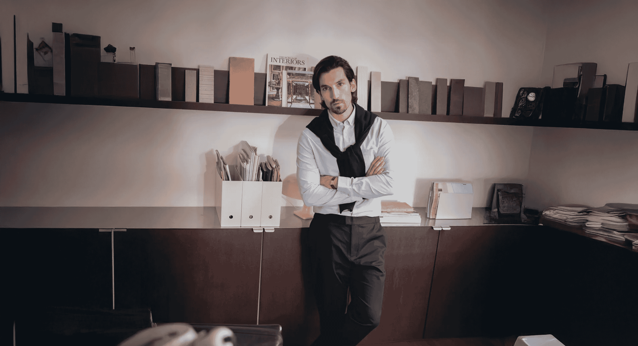 A man in a white dress shirt and black vest standing in a modern office.