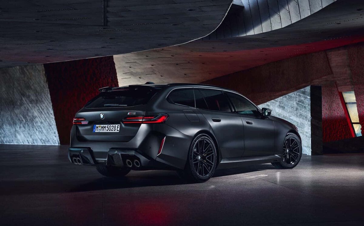 Matte black BMW M5 Touring in a concrete tunnel with dramatic red light accents highlighting its rear design.
