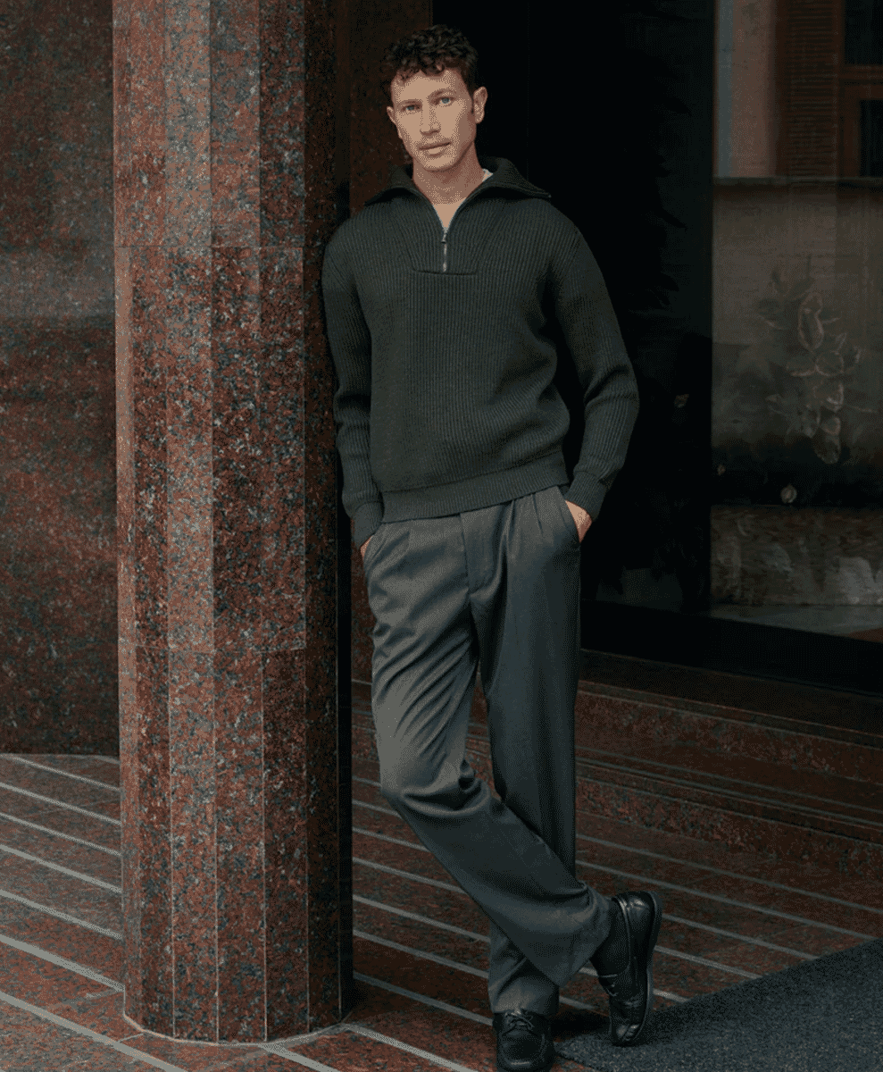 A man in a dark ribbed quarter-zip sweater leaning against a granite pillar.
