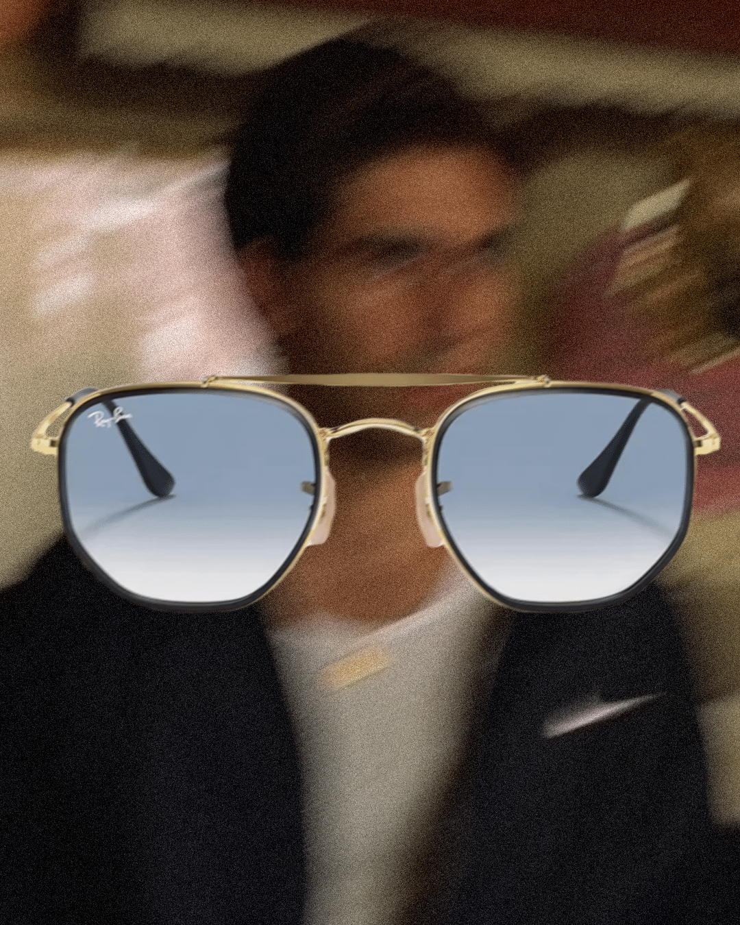 Man in a dark blazer and white shirt wearing gold-framed Ray-Ban sunglasses with gradient lenses.