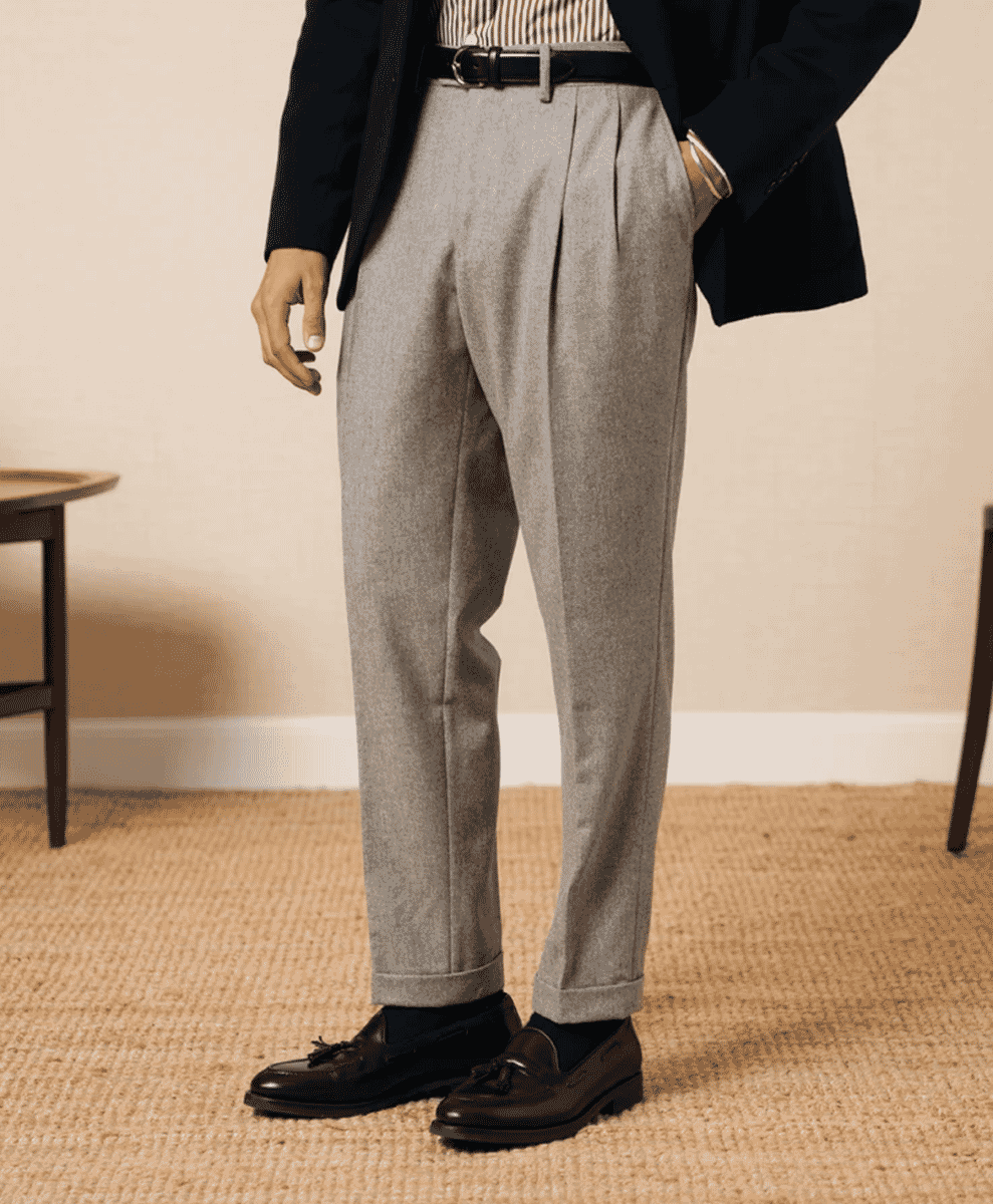 A man wearing grey pleated wool trousers with black tassel loafers.