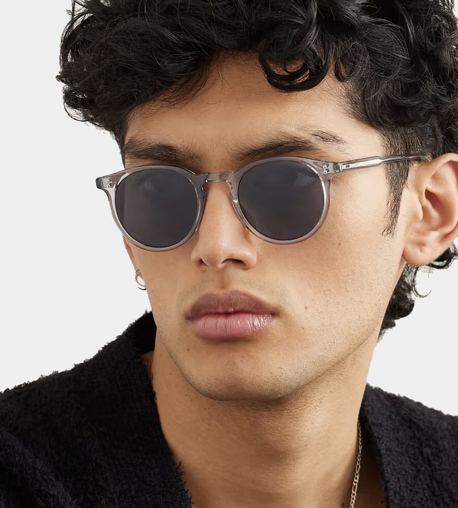 Man in a black textured sweater wearing round transparent-framed sunglasses.