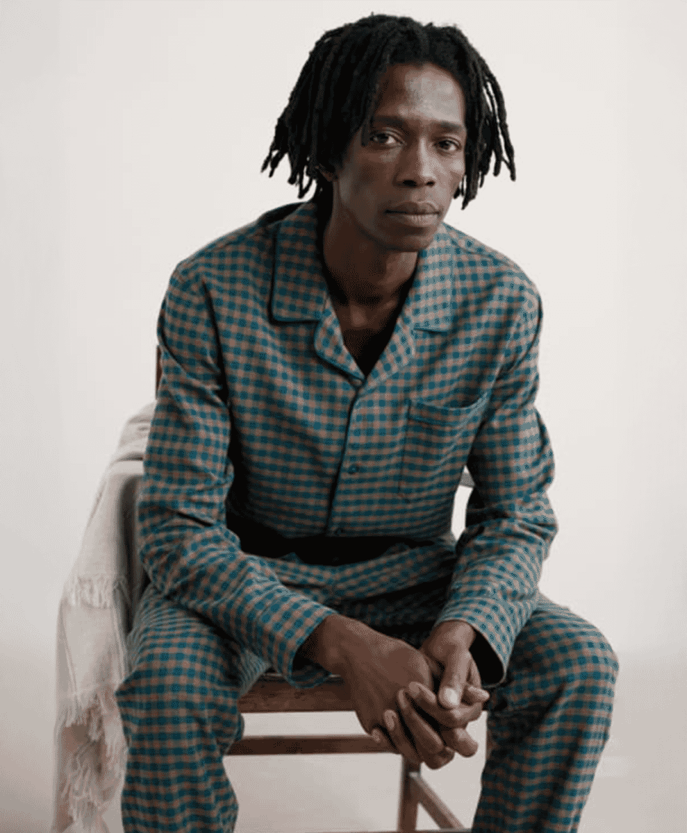 Man sitting in a wooden chair wearing a blue and beige checkered flannel pajama set.