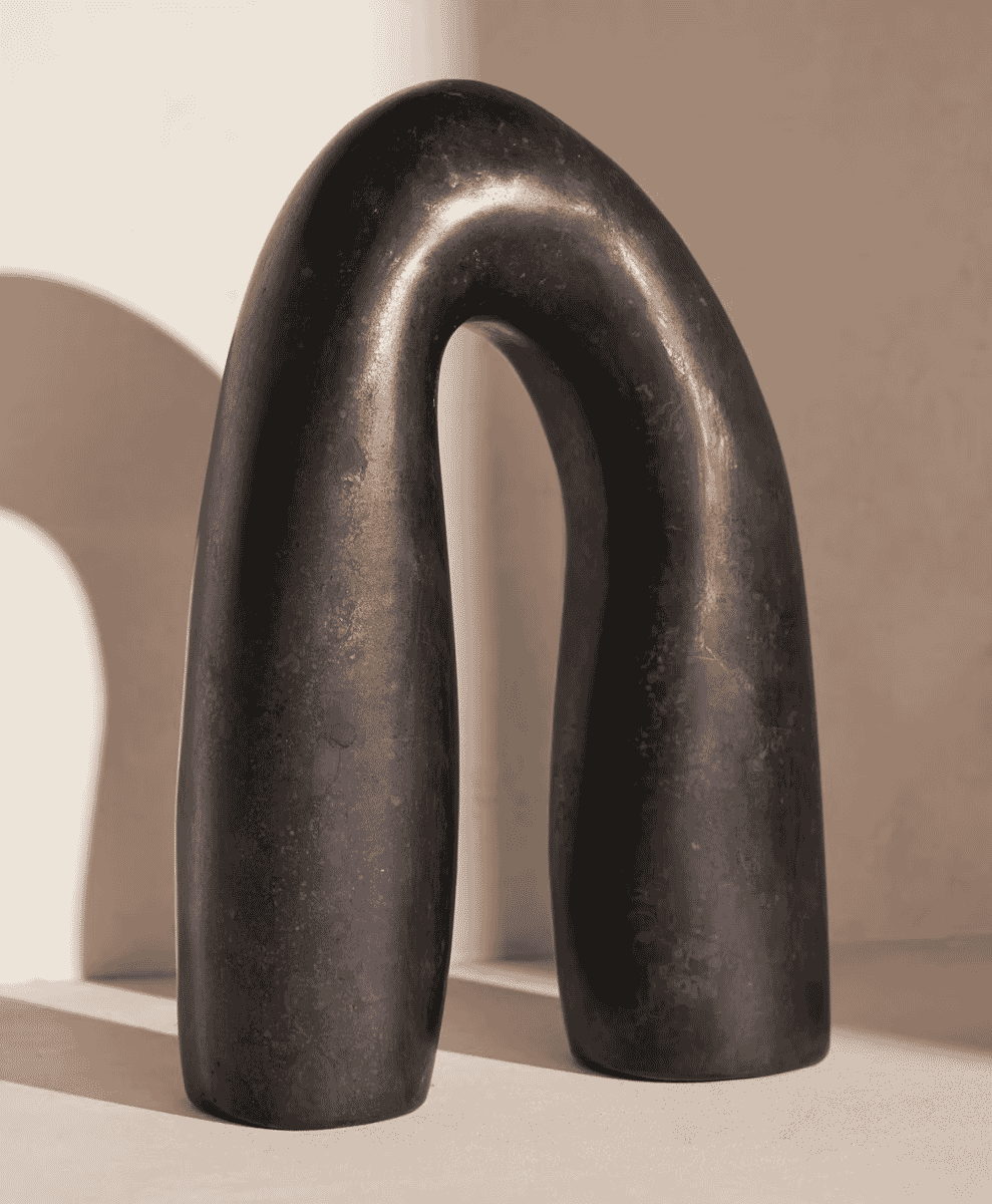 A dark, smooth abstract sculpture with curved lines in a minimalist setting.