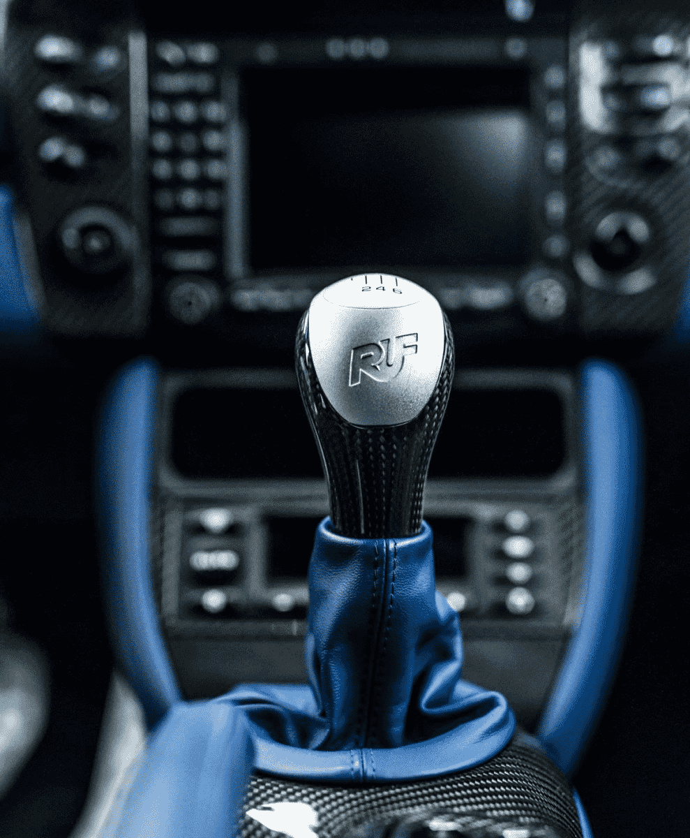 Close-up of a manual gear shift with blue leather and carbon fiber accents.