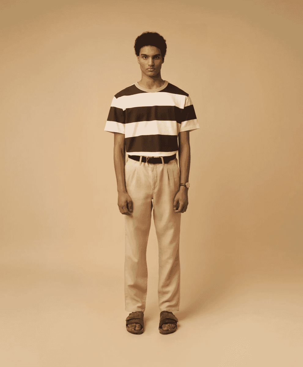 A man in a striped short-sleeve shirt and light-colored pleated trousers with a dark belt.