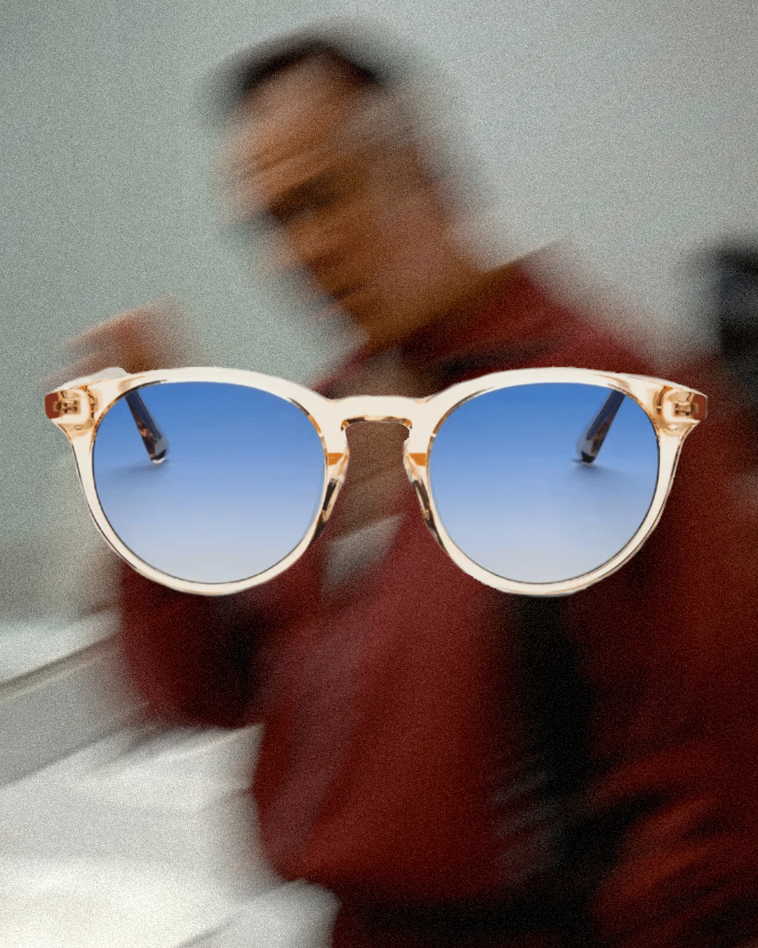 Close-up of round sunglasses featuring blue gradient lenses against a red background.