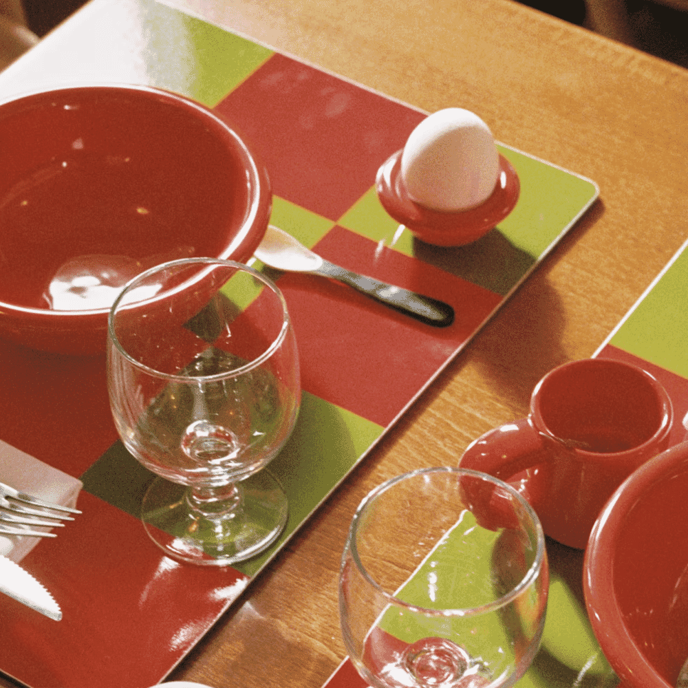 Close-up of red ceramic bowls and green and red checkered placemats on a modern dining table.
