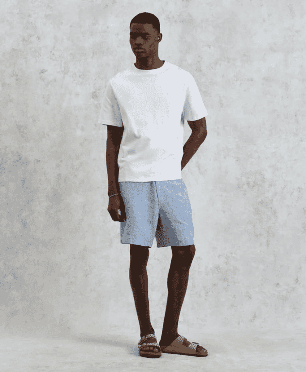 Man wearing a white t-shirt, light blue linen shorts, and brown sandals.