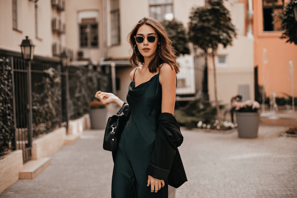 A woman in a dark green satin slip dress and a black blazer walking through an urban alleyway.