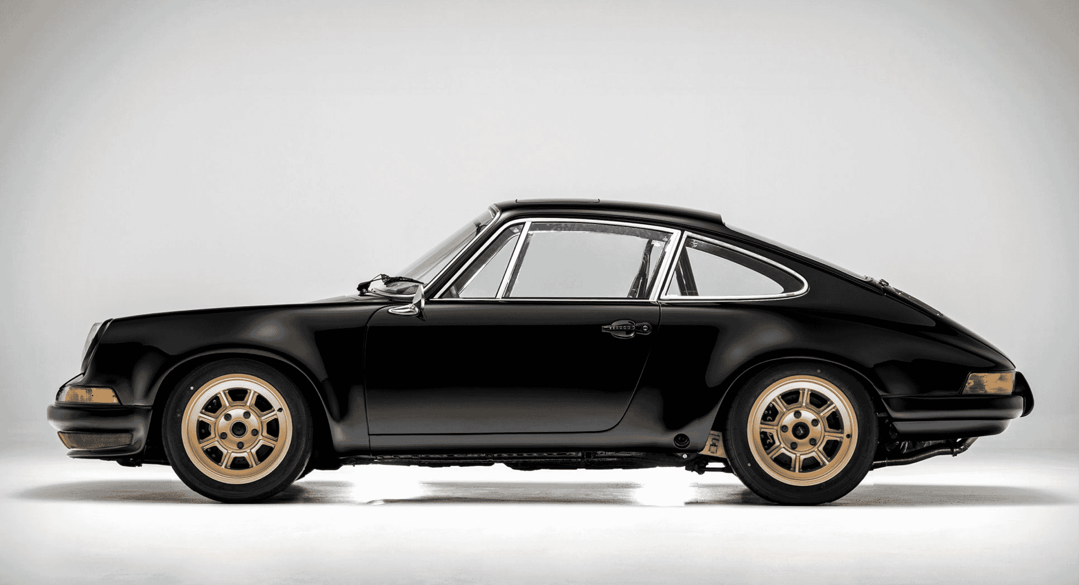 Profile view of a black Porsche sports car with gold rims in a studio.