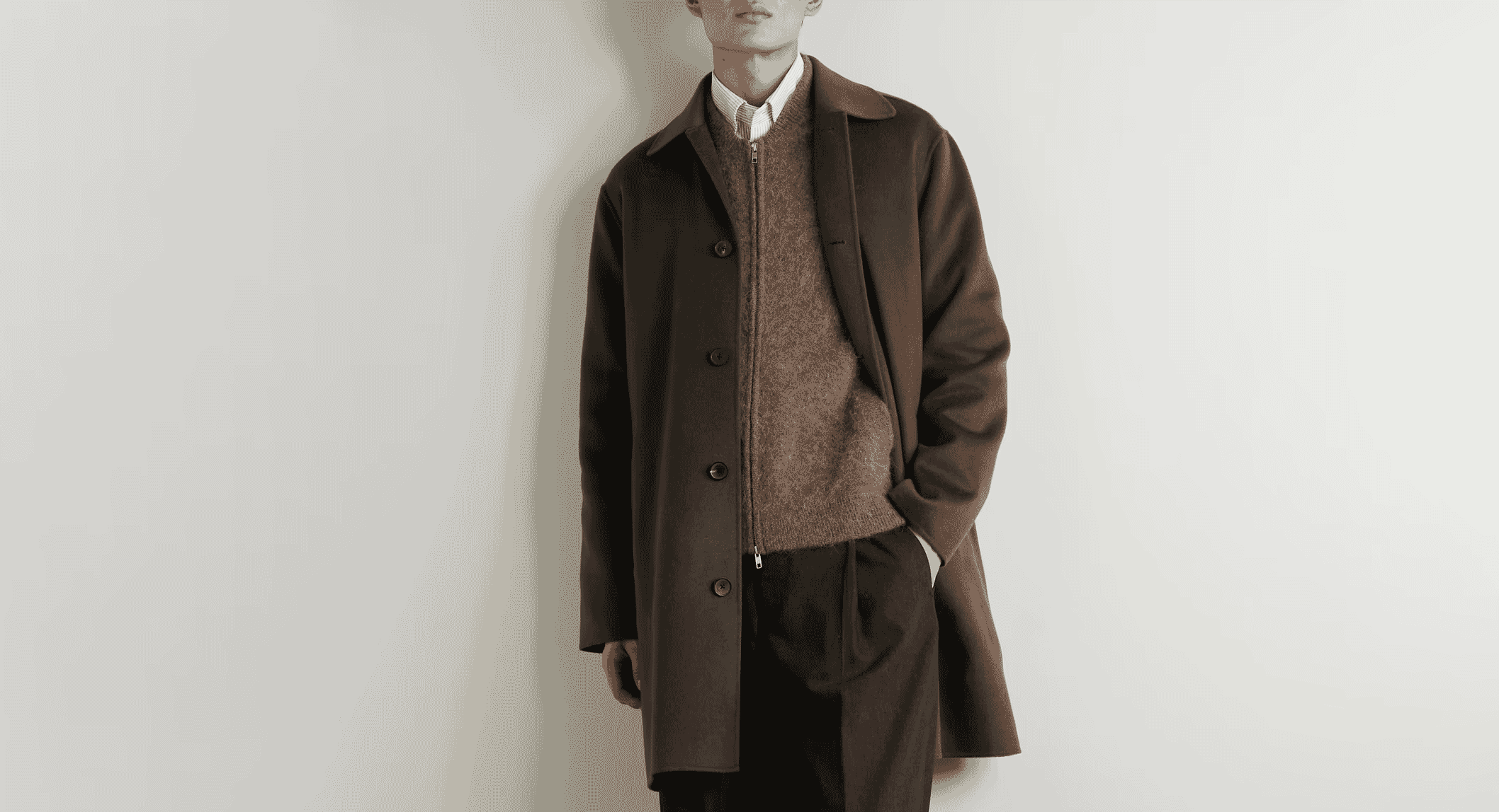 A man wearing a brown wool coat over a zip-front sweater and striped shirt.