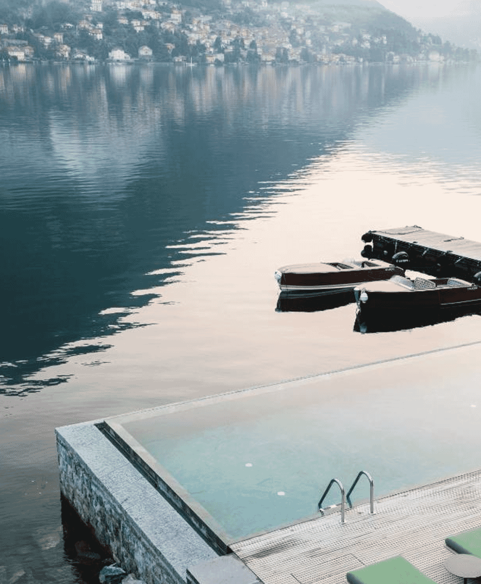 An infinity pool at Il Sereno with traditional wooden Riva boats docked at the private lakeside pier.