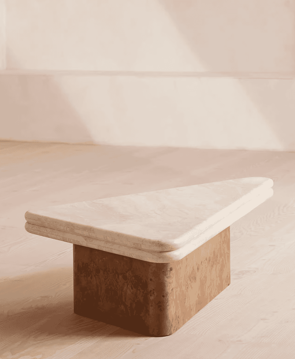 Minimalist triangular marble coffee table with a light veined top on a wooden floor.